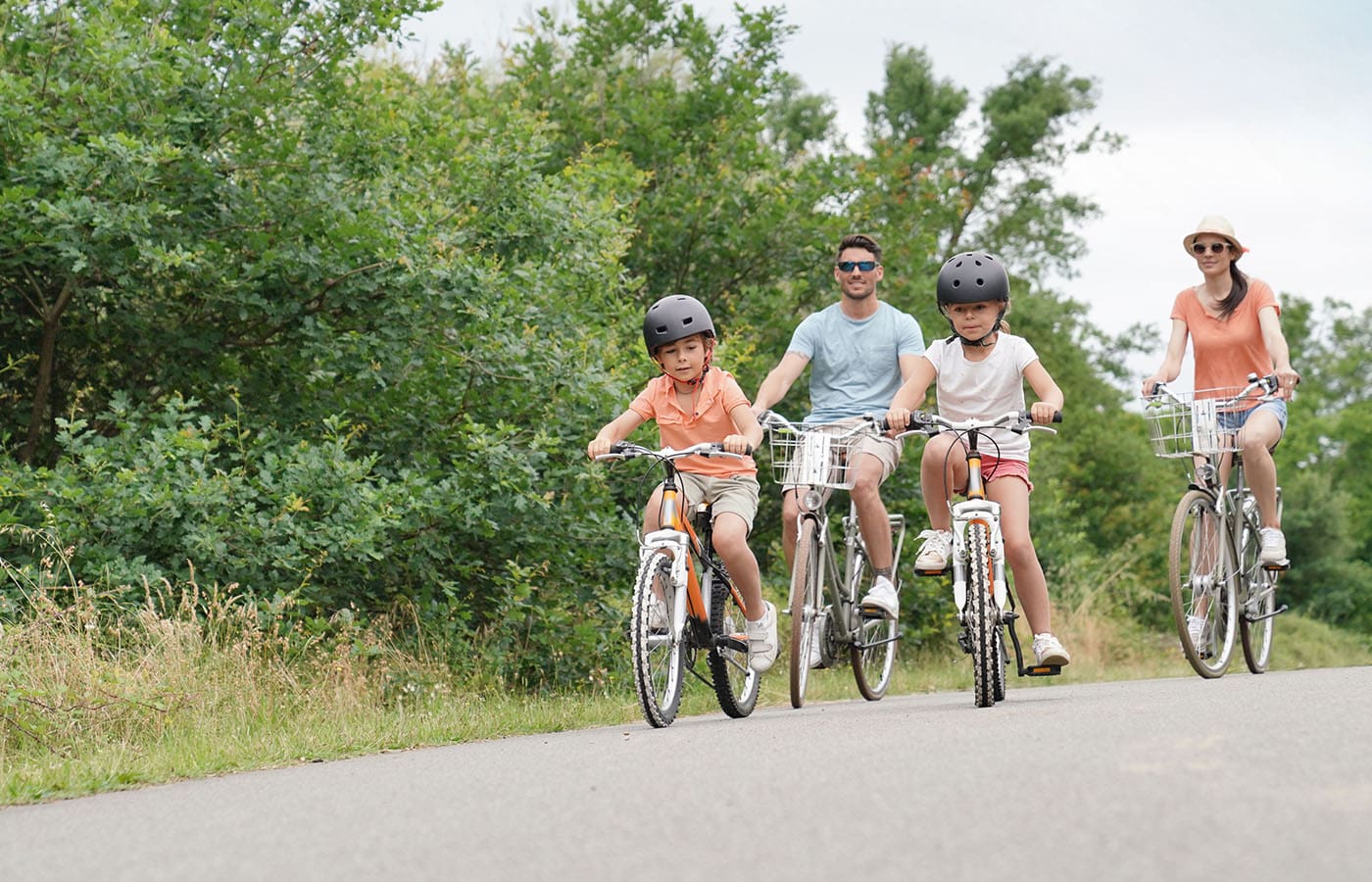 A woman serves breakfast to two smiling children and a man at a kitchen table set with pastries, oranges, berries, and glasses of orange juice.
