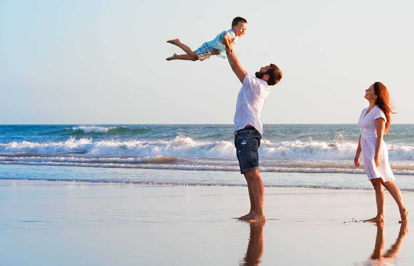 A young child and a woman smile with their faces touching gently in a sunlit room. The child wears a gray shirt with an animal graphic, and both appear joyful, sharing a tender and happy moment together.